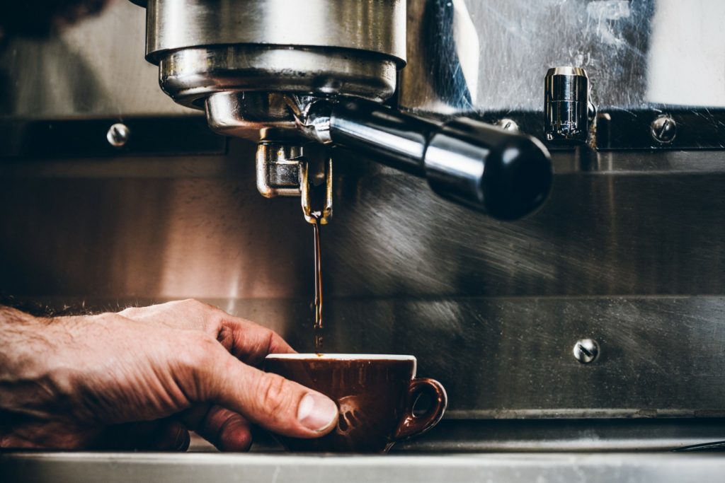 jak zrobić caffe latte - Męska dłoń trzyma filiżankę i nalewa kawę.